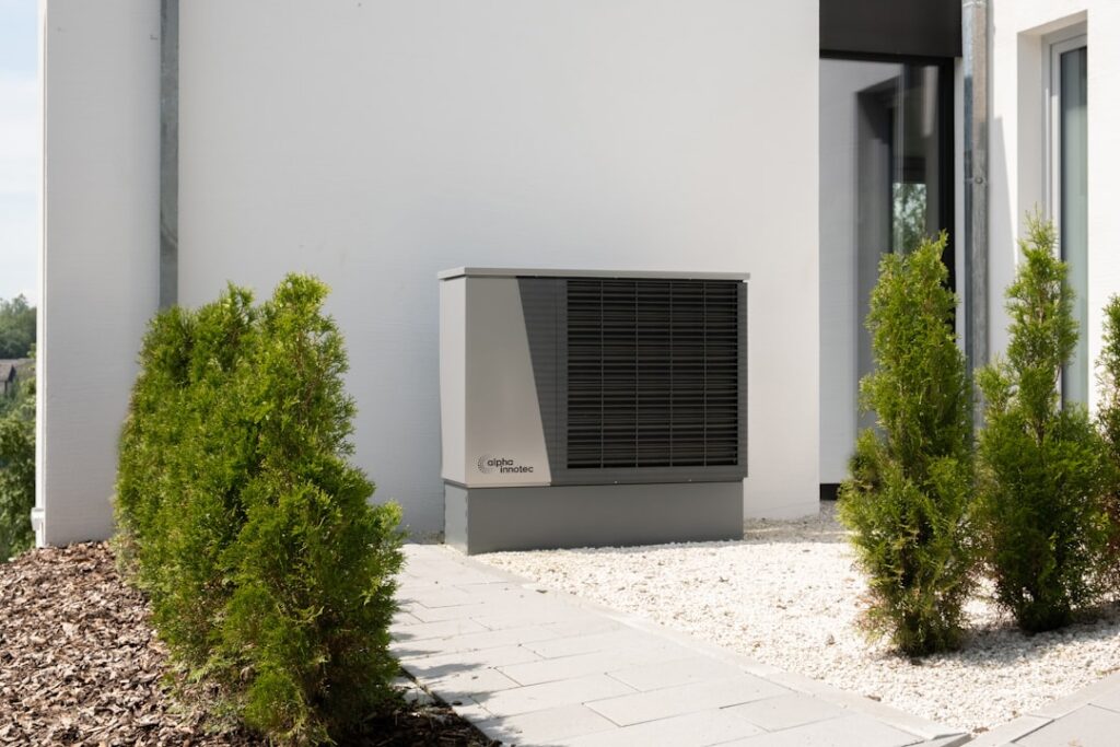 a-air-conditioner-sitting-on-the-side-of-a-building-nbwcvuifja Eine moderne Heizung mit Luft/Wasser Wärmepumpe im Garten.